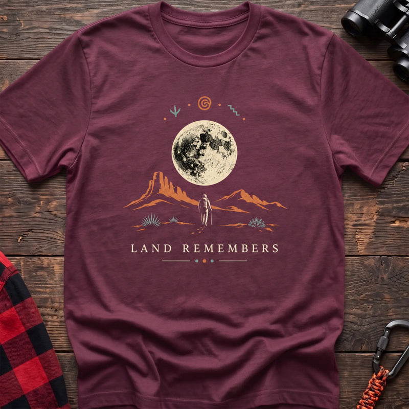 Heather maroon cotton t-shirt with a desert hiker and full moon graphic and Land Remembers text on rustic wood