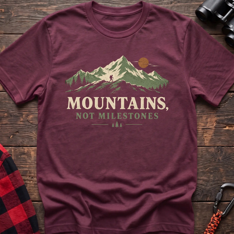 Heather maroon cotton t-shirt with a hiker and mountain graphic and Mountains Not Milestones text on rustic wood