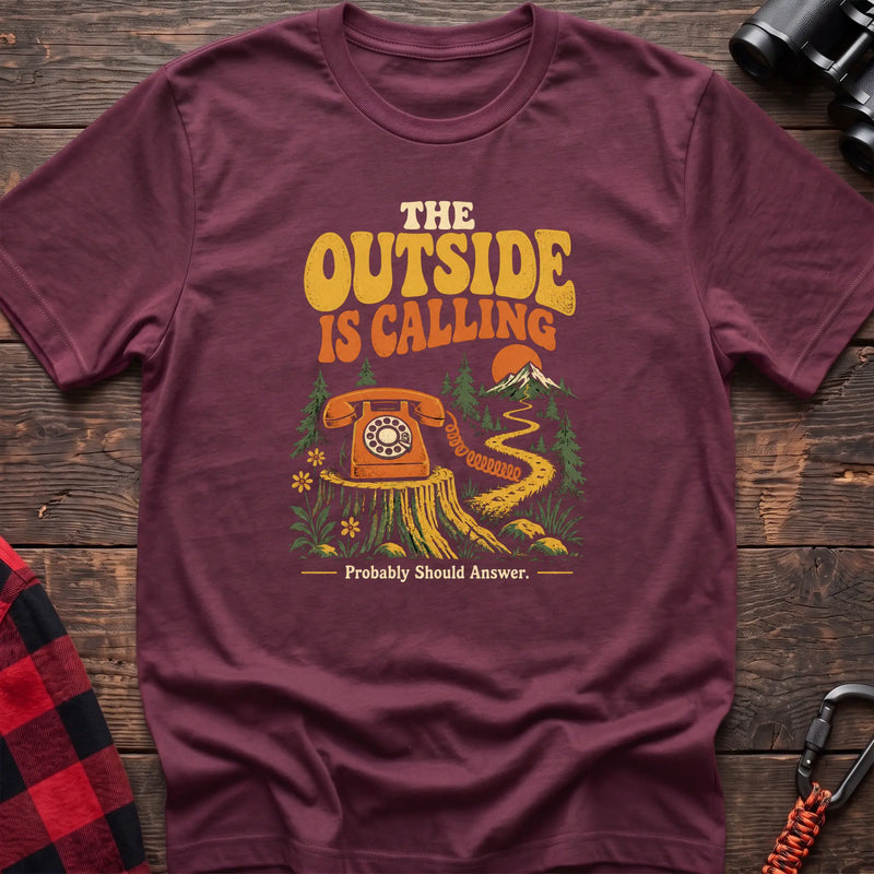 Heather maroon cotton t-shirt with a rotary phone on a stump graphic and The Outside Is Calling text on rustic wood