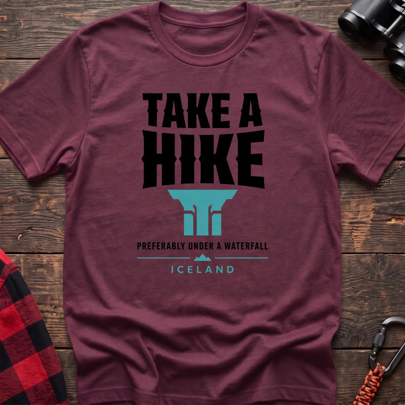 Heather maroon cotton t-shirt with a waterfall graphic and Take a Hike Preferably Under a Waterfall Iceland text on rustic wood