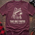 Heather maroon cotton t-shirt with a raccoon graphic and Take Only Photos Leave the Snacks text on rustic wood