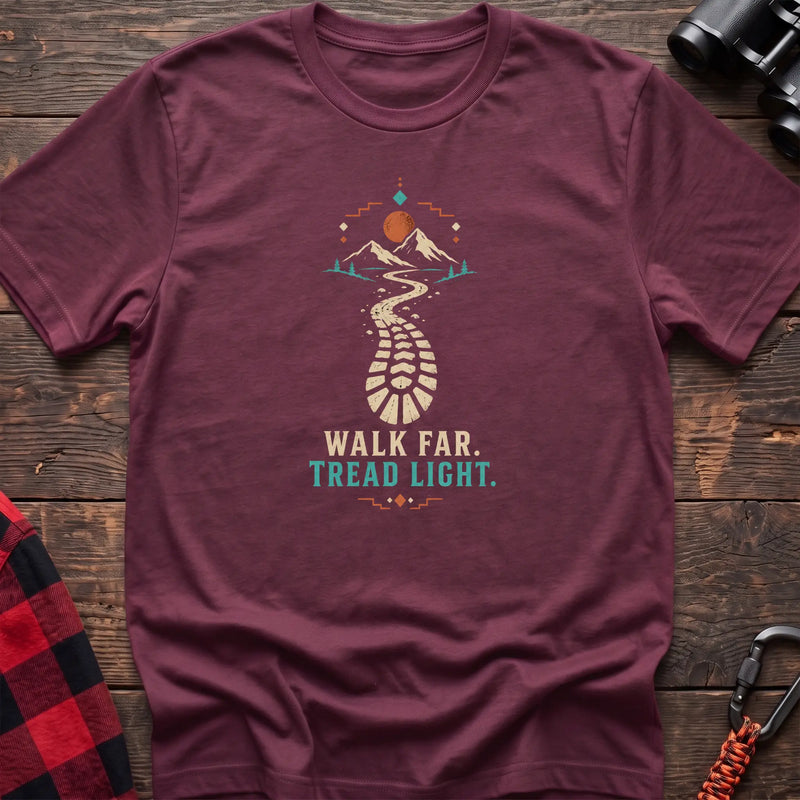 Heather maroon cotton t-shirt with a bootprint trail and mountain graphic and Walk Far Tread Light text on rustic wood