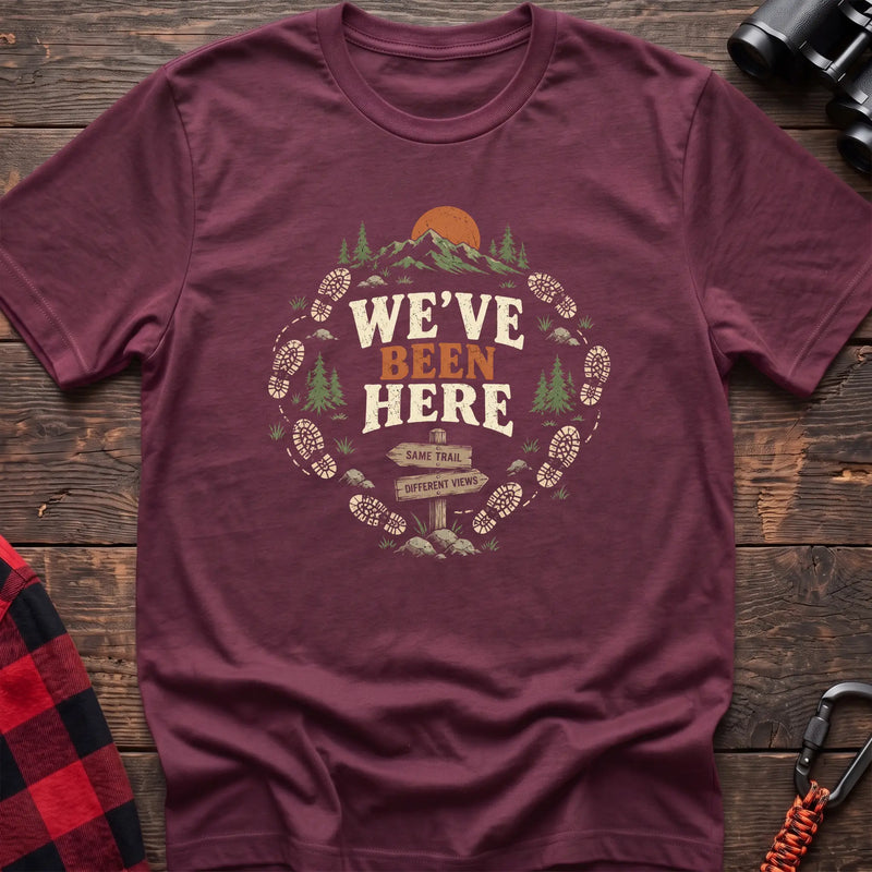 Heather maroon cotton t-shirt with a bootprint circle and trail sign graphic and We’ve Been Here text on rustic wood