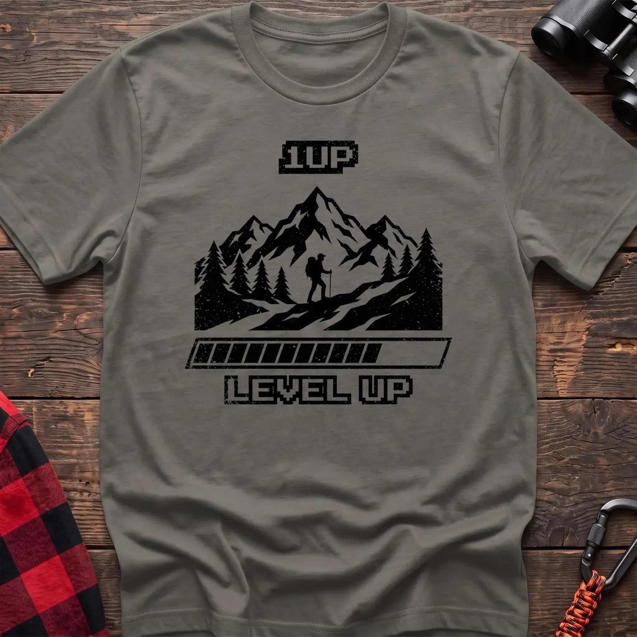 Heather military green t-shirt with black graphic of a hiker on a mountain trail under pixel-style 1UP text and a progress bar reading Level Up