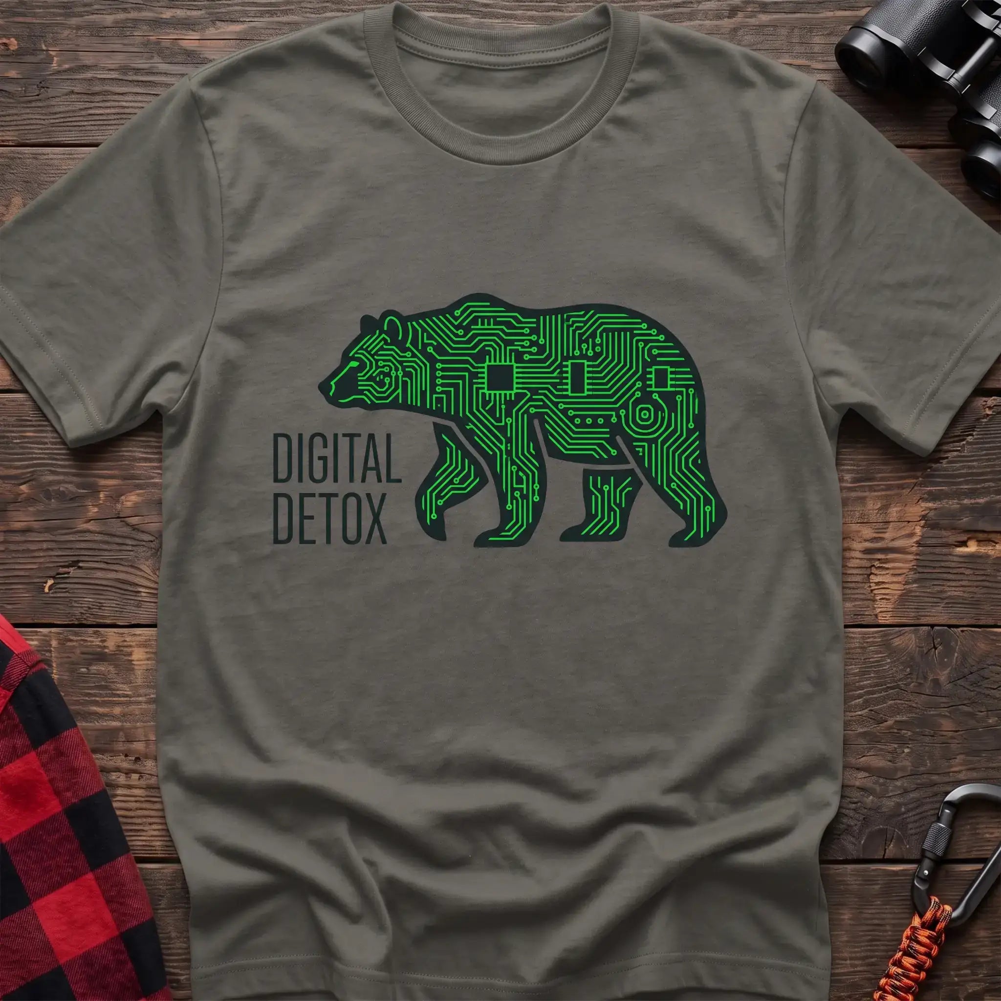 Heather military green t-shirt with a neon green circuit-board patterned silhouette of a walking bear, and the text “DIGITAL DETOX” printed to the left of the design, laid flat on a wooden surface.
