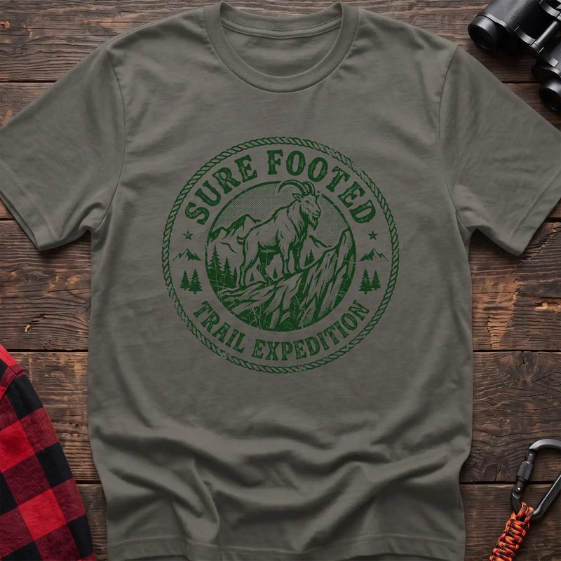 Heather military green t-shirt with circular badge graphic of a mountain goat on a rocky peak reading Sure Footed Trail Expedition