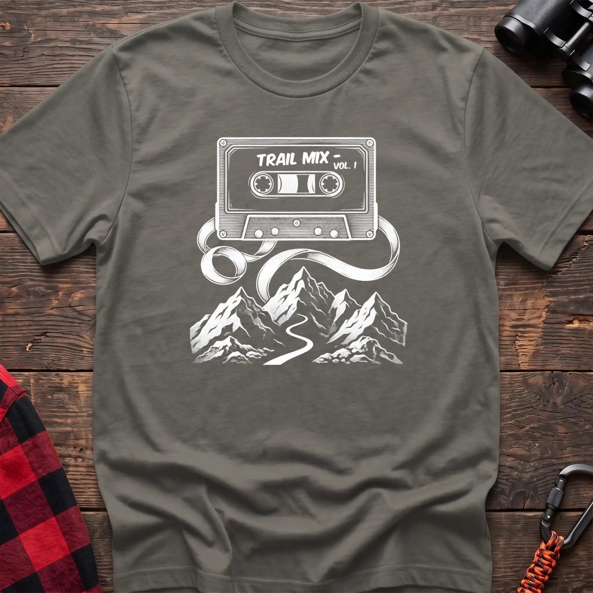 Heather military green t-shirt with white cassette tape graphic labeled Trail Mix Vol. 1, with tape unspooling into a trail through mountains