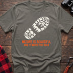 Heather military green t-shirt with white boot print graphic featuring a skull and pine trees, and orange text reading Nature Is Beautiful And It Wants You Dead