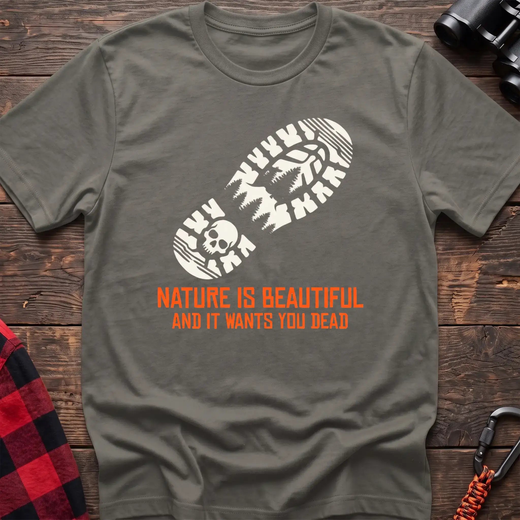 Heather military green t-shirt with white boot print graphic featuring a skull and pine trees, and orange text reading Nature Is Beautiful And It Wants You Dead