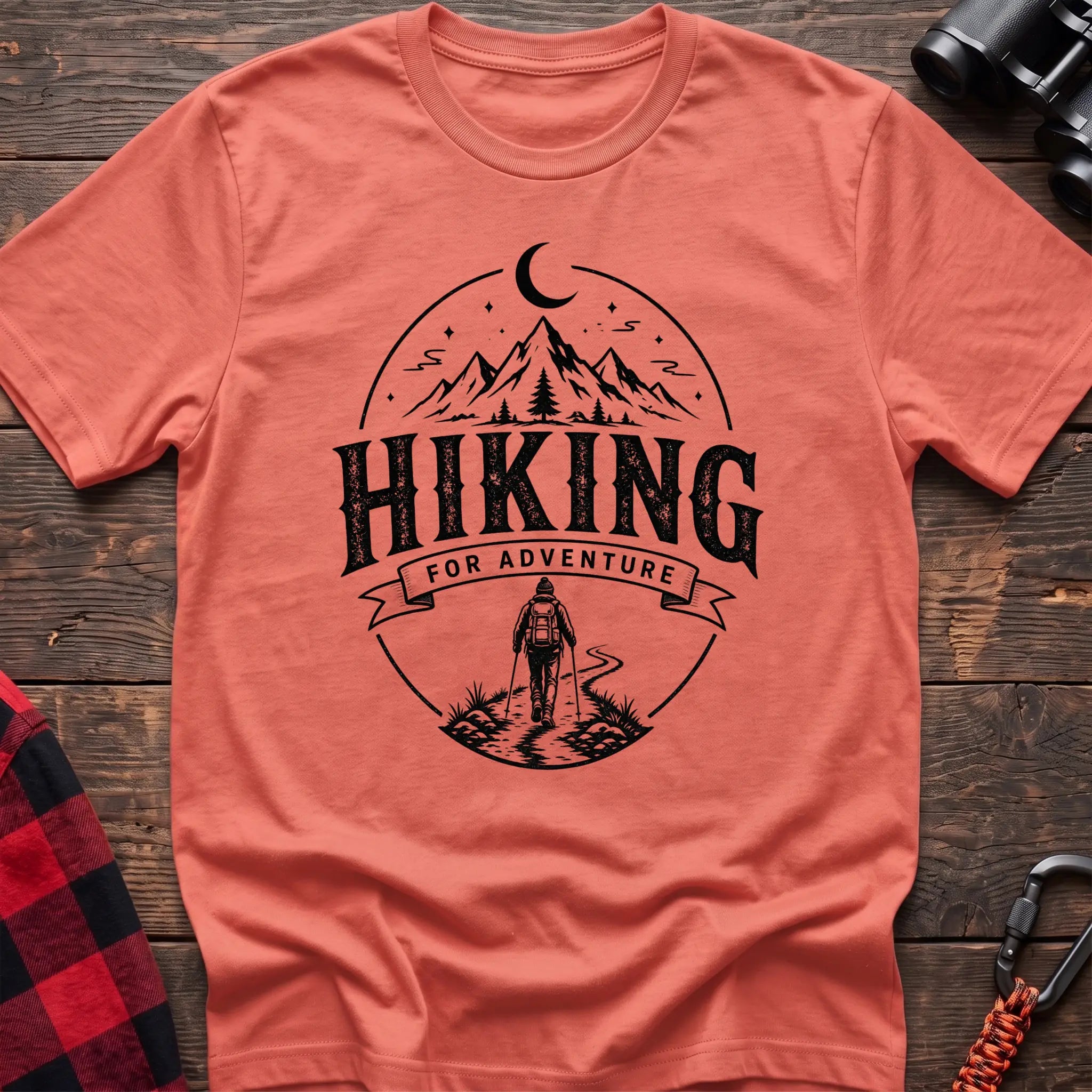 Heather orange cotton t-shirt with vintage Hiking for Adventure graphic of mountains under a crescent moon and a hiker on a trail, flat lay on rustic wood with hiking gear