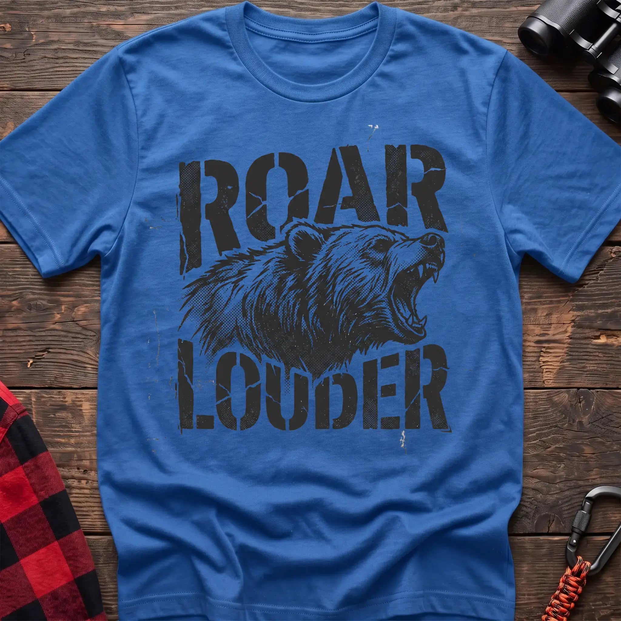 Heather royal t-shirt with a distressed black graphic of a roaring bear head between the bold text “ROAR” and “LOUDER,” laid flat on a wooden surface.