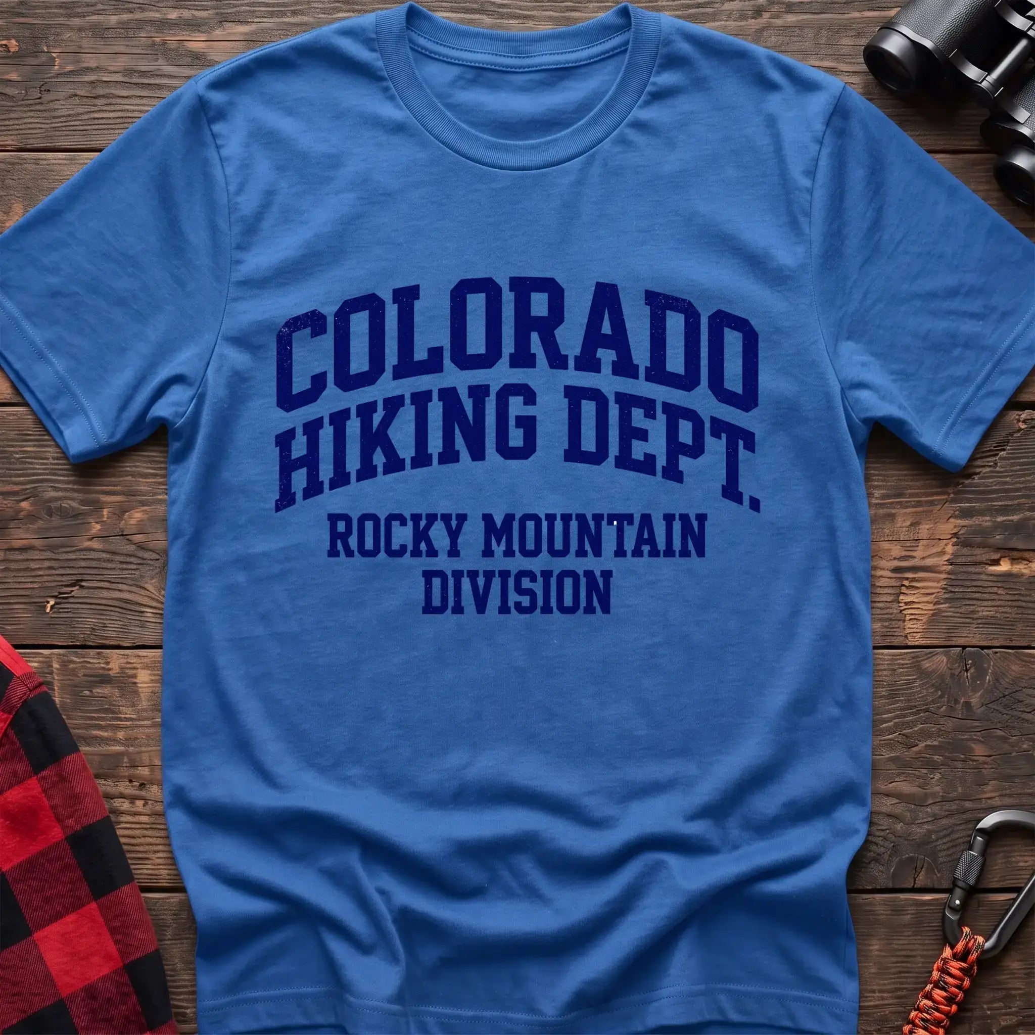 Heather royal t-shirt with distressed dark blue collegiate-style text reading “COLORADO HIKING DEPT. ROCKY MOUNTAIN DIVISION,” laid flat on a wooden surface.
