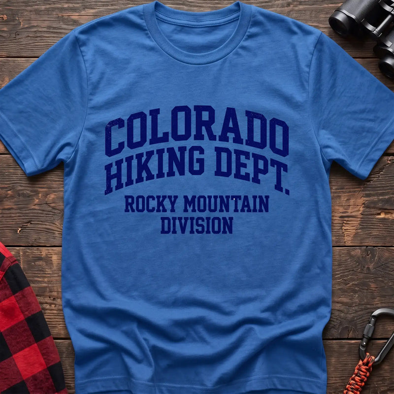 Heather royal t-shirt with distressed dark blue collegiate-style text reading “COLORADO HIKING DEPT. ROCKY MOUNTAIN DIVISION,” laid flat on a wooden surface.
