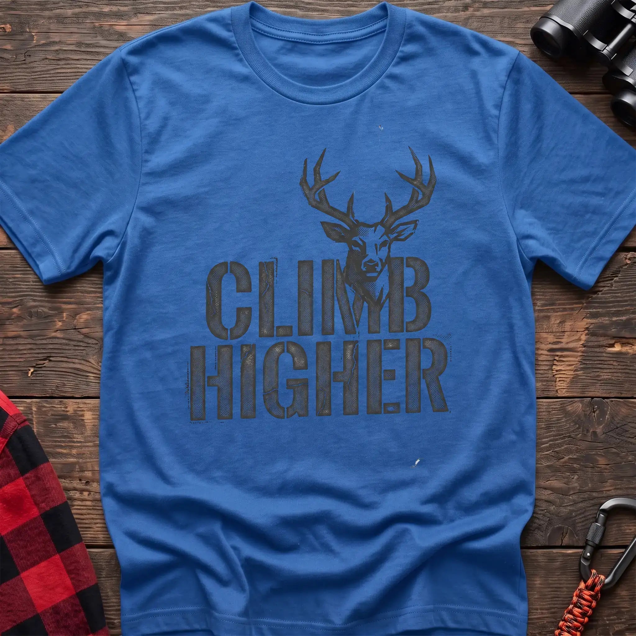 Heather royal t-shirt with a distressed dark graphic of a deer’s head and antlers rising from the bold text “CLIMB HIGHER,” laid flat on a wooden surface.