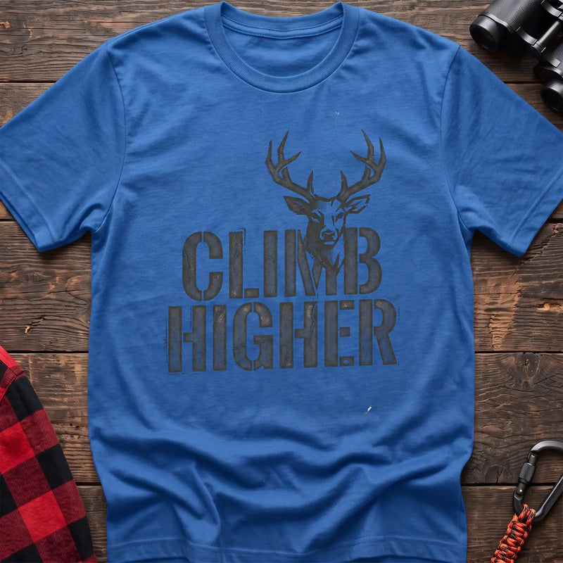 Heather royal t-shirt with a distressed dark graphic of a deer’s head and antlers rising from the bold text “CLIMB HIGHER,” laid flat on a wooden surface.