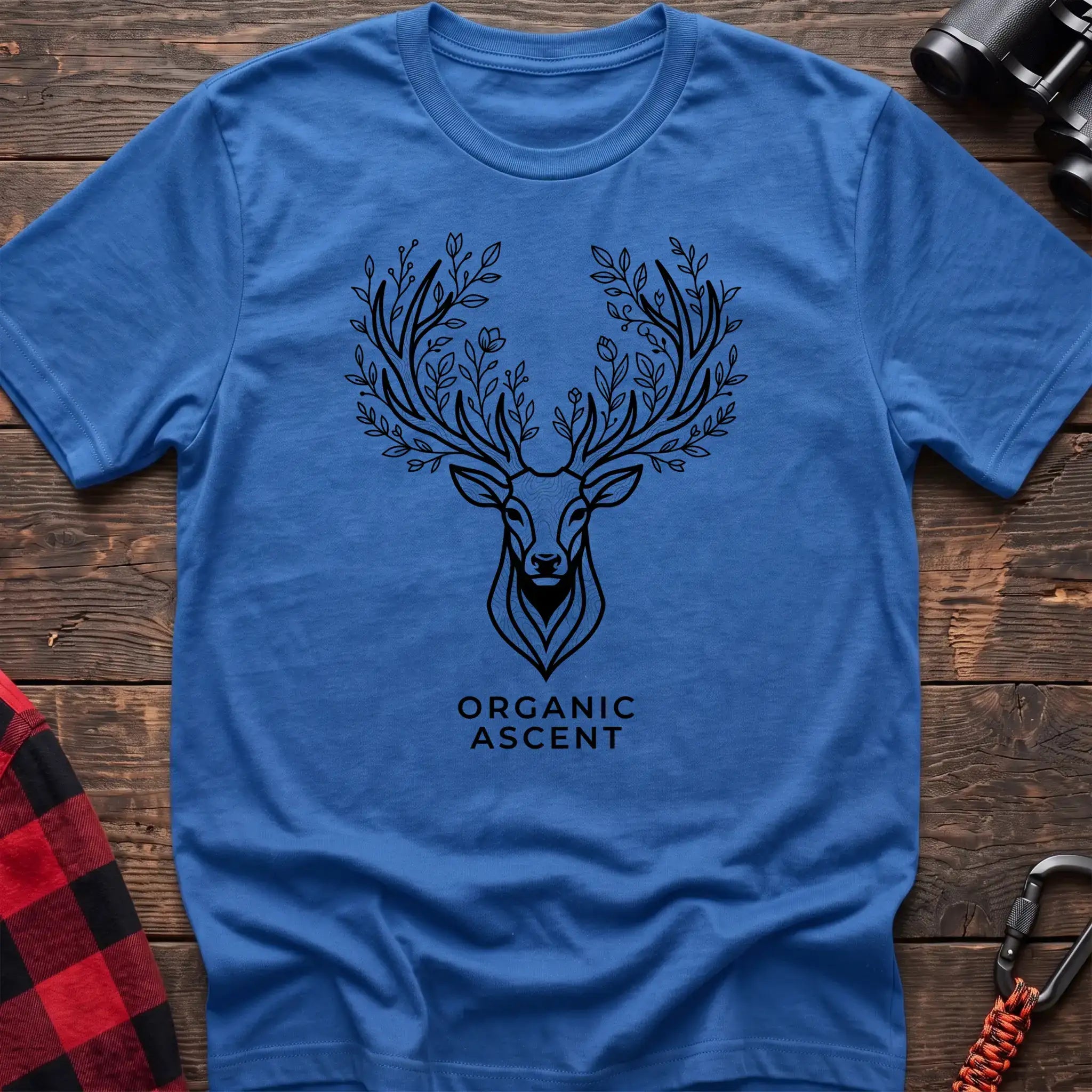 Heather royal t-shirt with a black line drawing of a deer’s head whose antlers are formed from leafy branches and flowers, with the text “ORGANIC ASCENT” printed below, laid flat on a wooden surface.