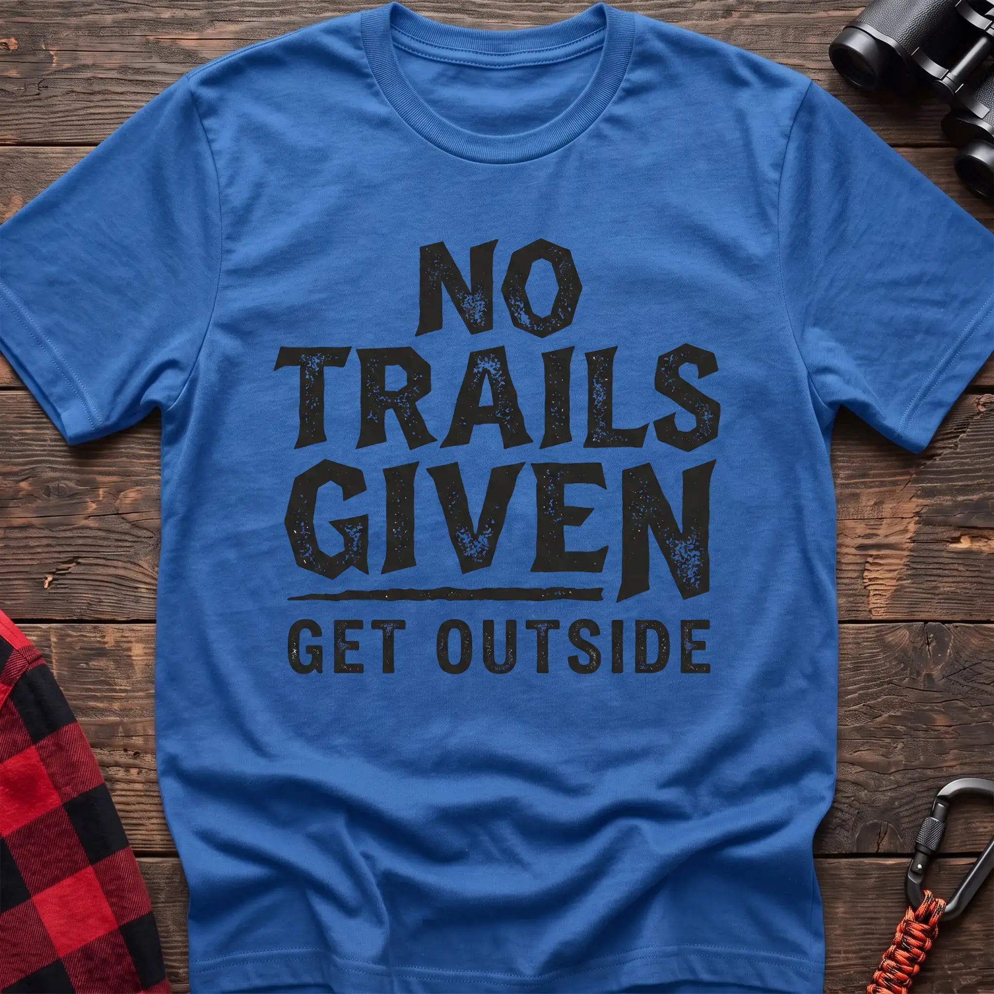 Heather royal t-shirt with distressed black text reading “NO TRAILS GIVEN” and “GET OUTSIDE” below it, laid flat on a wooden surface.