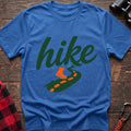 Heather royal cotton t-shirt with green cursive hike script, orange hiking boot, and footprint trail graphic, flat lay on rustic wood with hiking gear