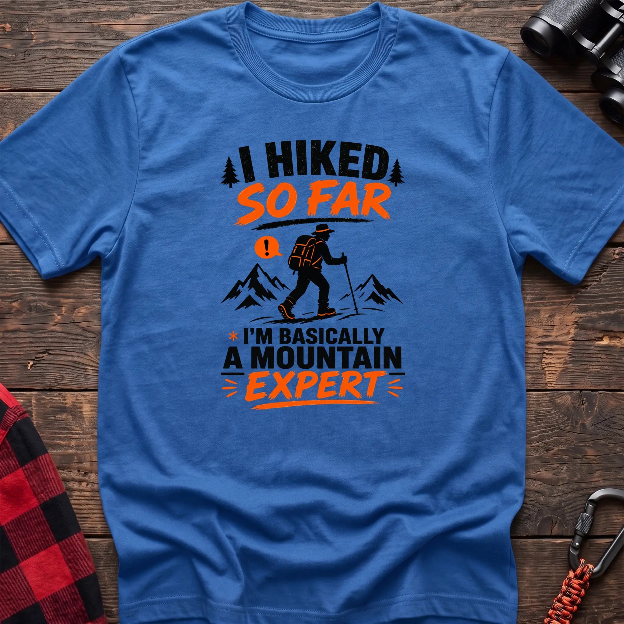 Heather royal cotton t-shirt with I Hiked So Far I'm Basically a Mountain Expert graphic of a hiker with backpack and trekking pole, flat lay on rustic wood with hiking gear