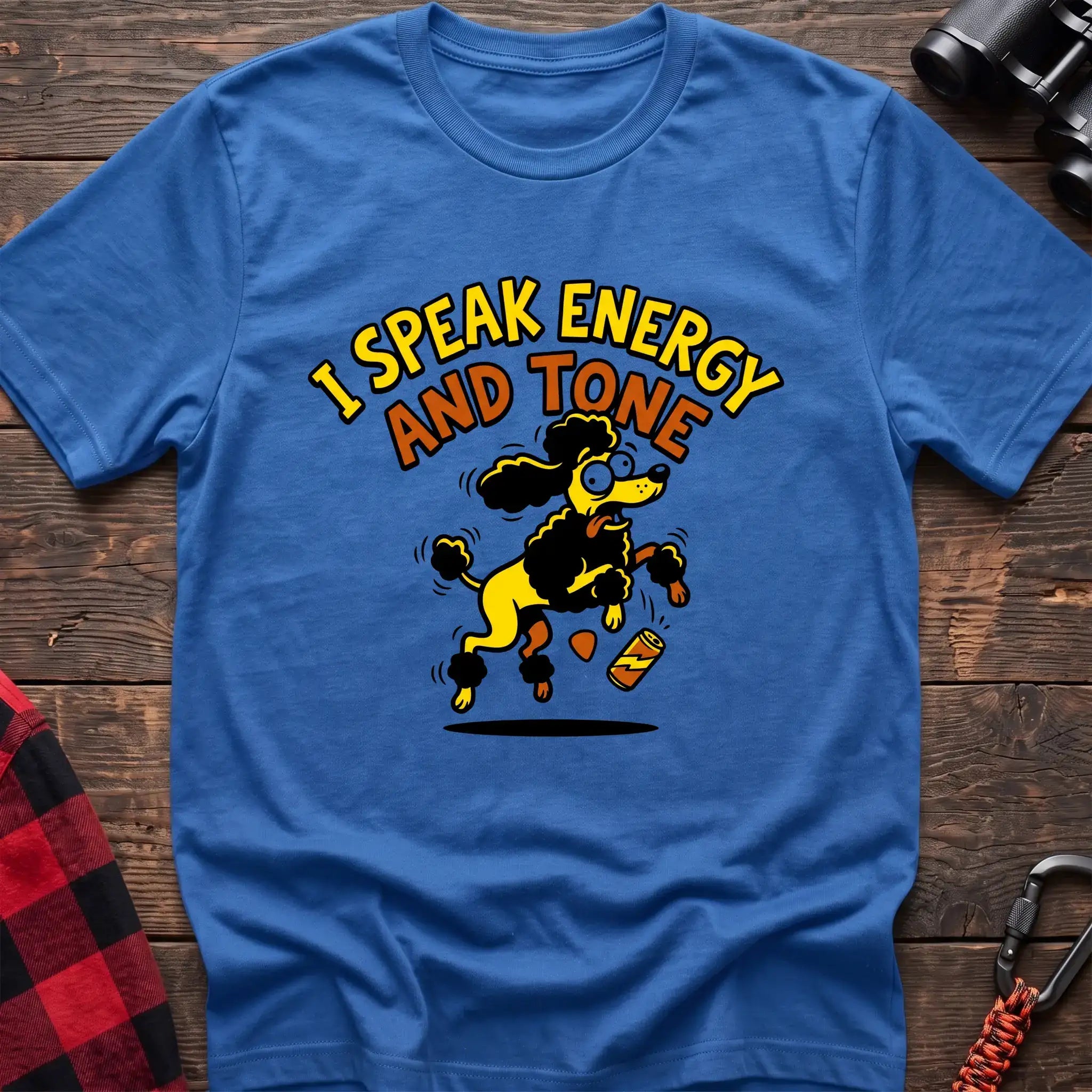 Heather royal t-shirt with a cartoon yellow and black poodle jumping excitedly next to a falling energy drink can, with the arched text “I SPEAK ENERGY AND TONE,” laid flat on a wooden surface.