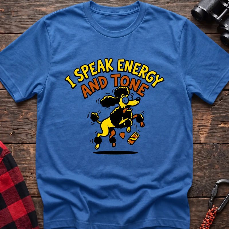 Heather royal t-shirt with a cartoon yellow and black poodle jumping excitedly next to a falling energy drink can, with the arched text “I SPEAK ENERGY AND TONE,” laid flat on a wooden surface.