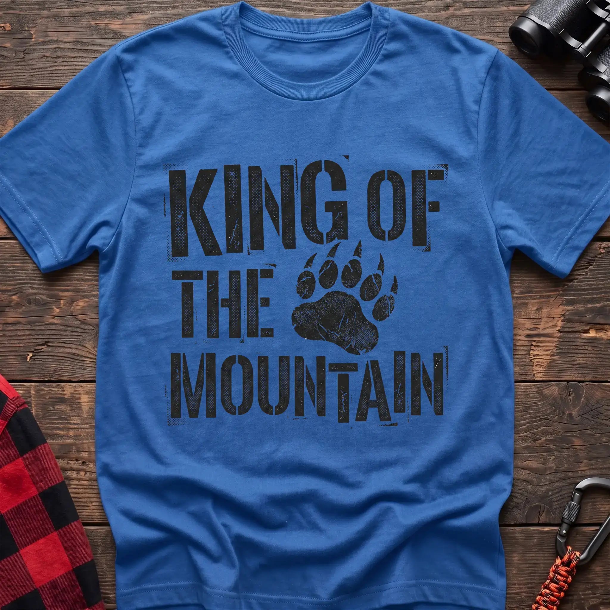 Heather royal t-shirt with distressed black text reading “KING OF THE MOUNTAIN” and a large bear paw print integrated into the design, laid flat on a wooden surface.