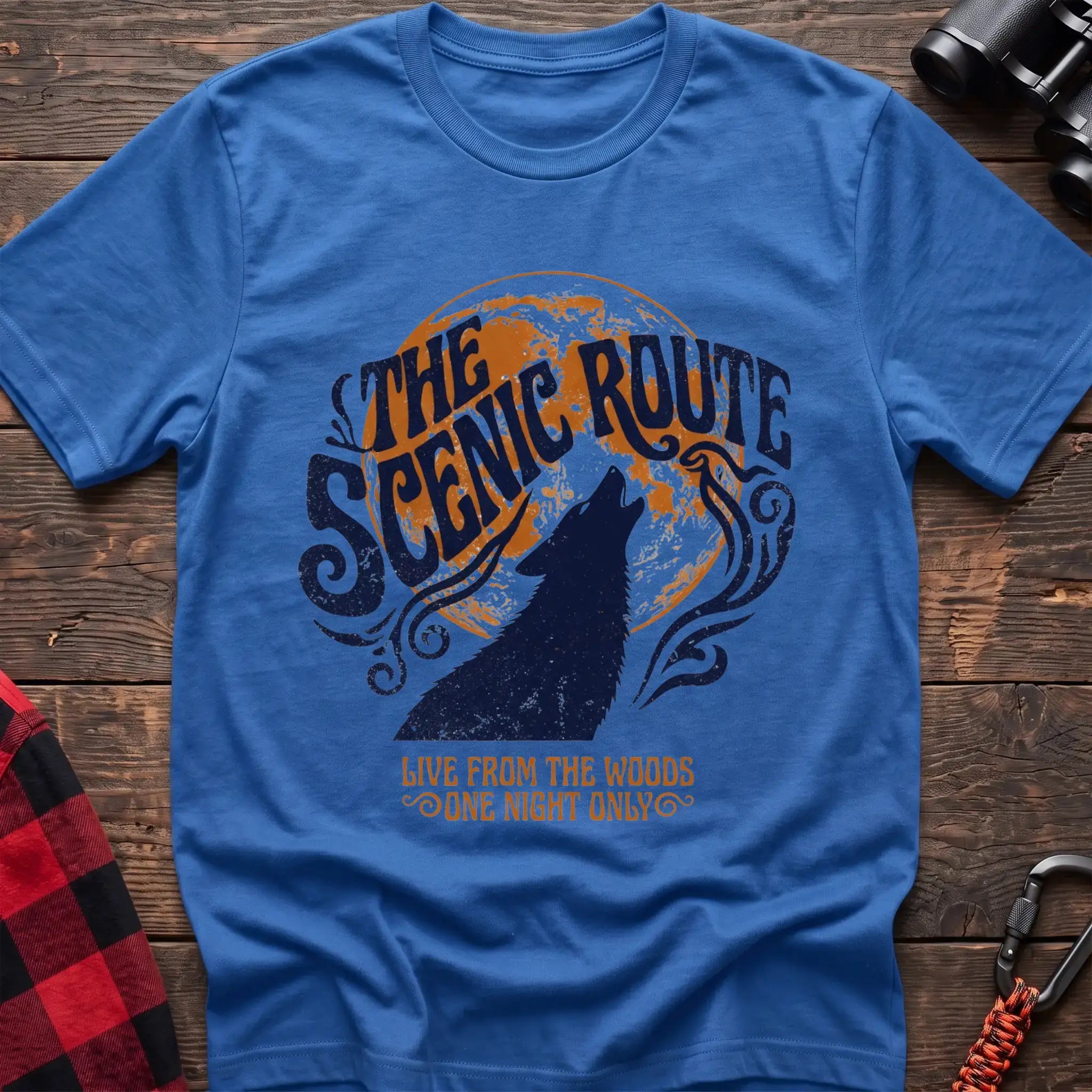 Heather royal t-shirt with a dark blue howling wolf silhouette against an orange circle, with the arched text “THE SCENIC ROUTE” above and “LIVE FROM THE WOODS / ONE NIGHT ONLY” below, laid flat on a wooden surface.
