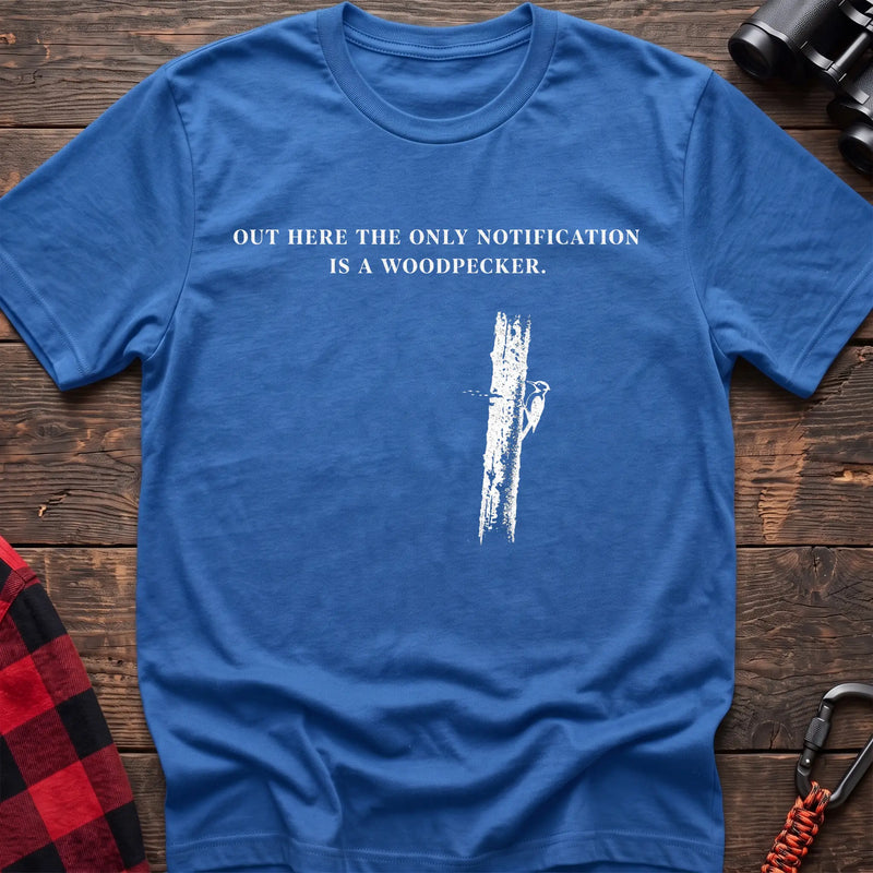 Heather royal cotton t-shirt with a woodpecker graphic and Out Here the Only Notification Is a Woodpecker text on rustic wood