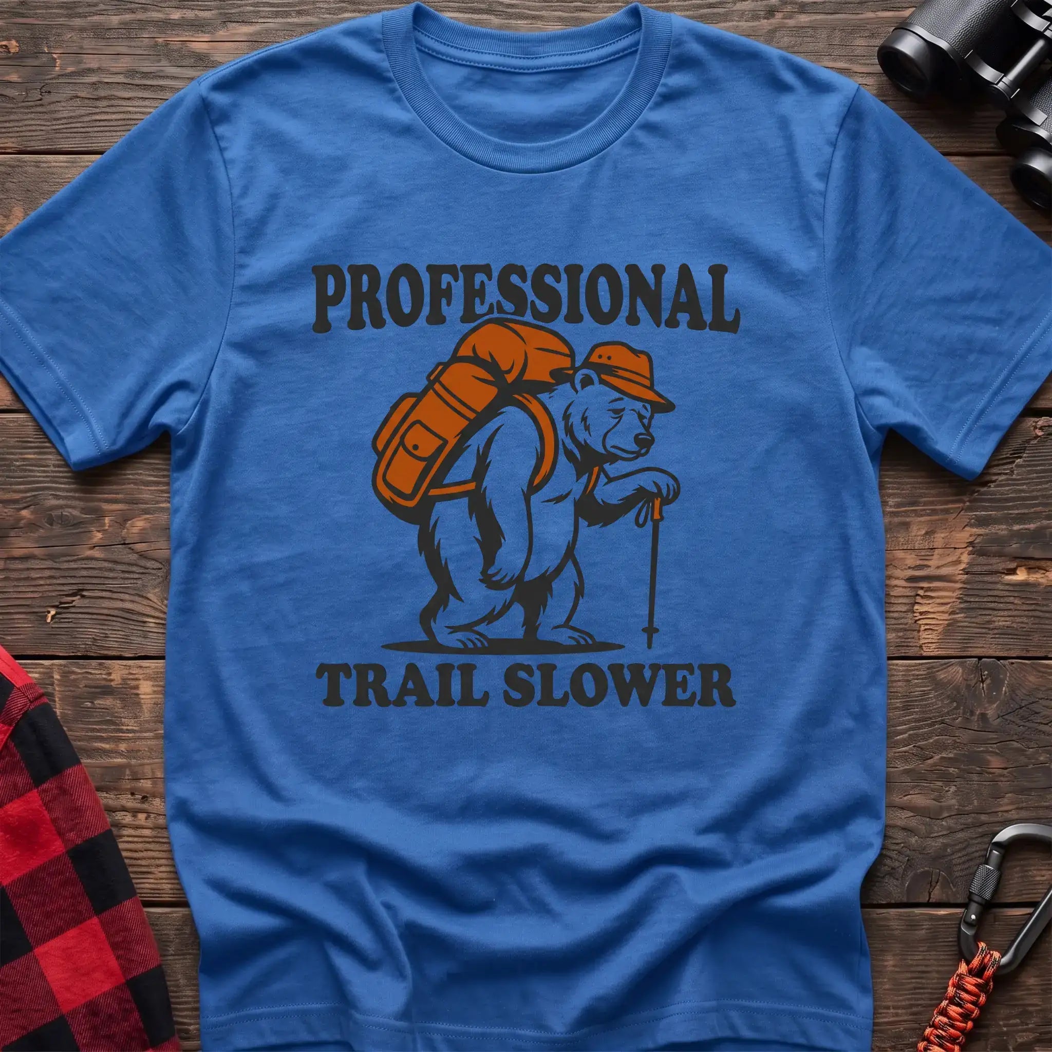 Heather royal t-shirt with a cartoon polar bear wearing a backpack and hat while holding a hiking stick, with the text “PROFESSIONAL TRAIL SLOWER,” laid flat on a wooden surface.