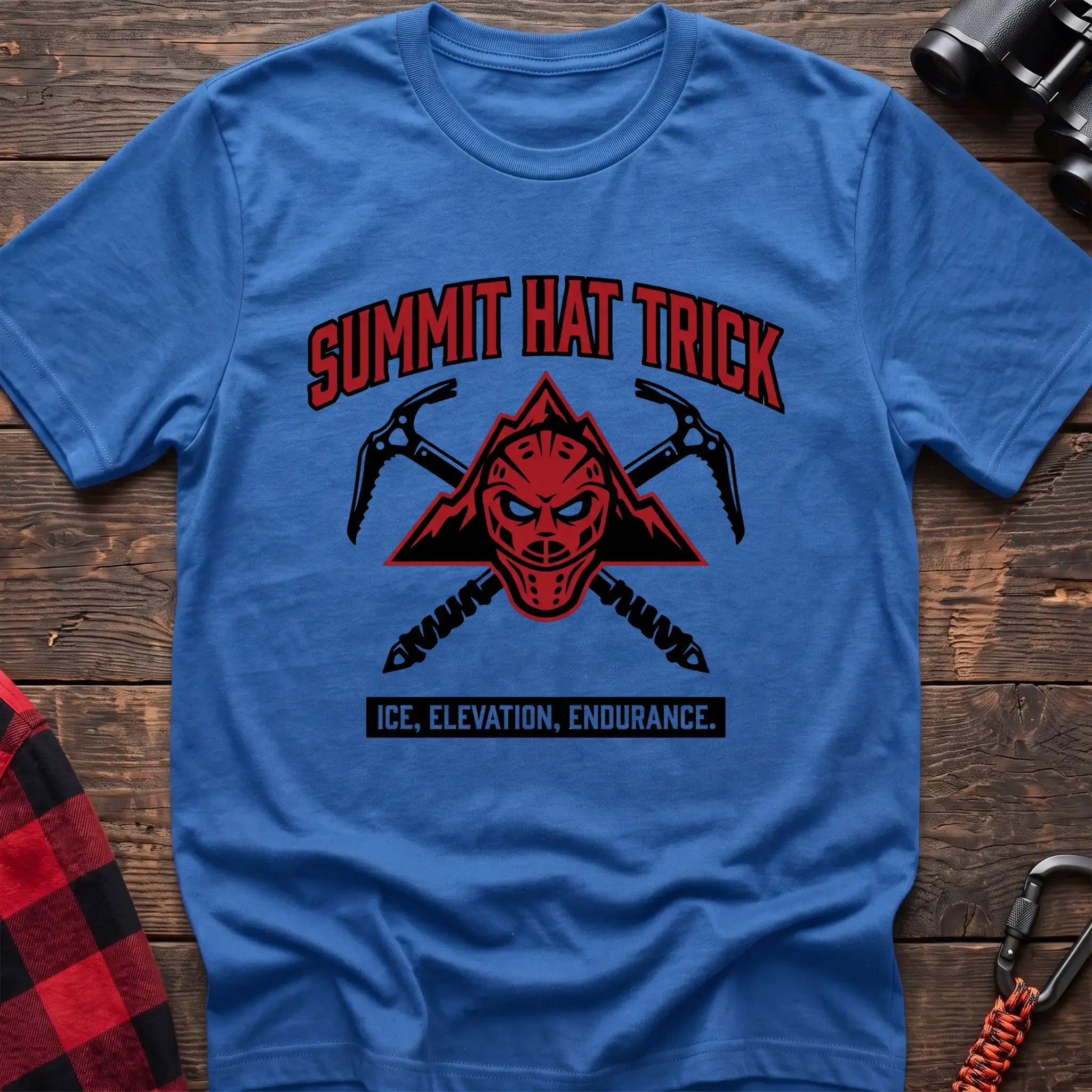 Heather royal t-shirt with a red mountain-themed goalie mask and crossed ice axes, with the text “SUMMIT HAT TRICK” and “ICE, ELEVATION, ENDURANCE,” laid flat on a wooden surface.