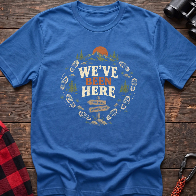 Heather royal cotton t-shirt with a bootprint circle and trail sign graphic and We’ve Been Here text on rustic wood