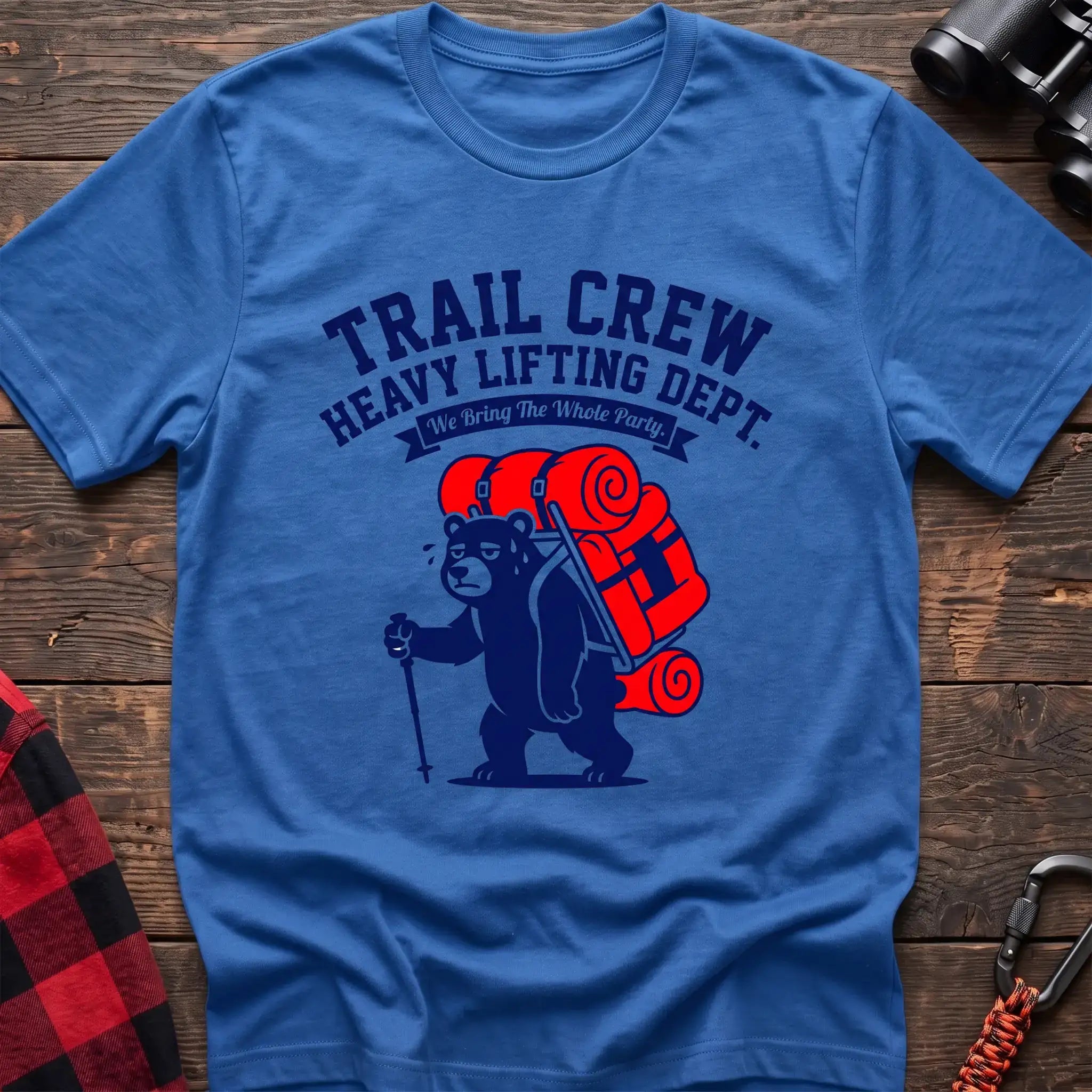 Heather royal t-shirt with a cartoon dark blue bear carrying a large red backpack and hiking pole, with the text “TRAIL CREW HEAVY LIFTING DEPT. We Bring The Whole Party,” laid flat on a wooden surface.