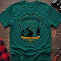Kelly green cotton hiking t-shirt with Unmarked Trail Society badge, winding trail, mountains, pine trees, and "Members Get Lost on Purpose" text
