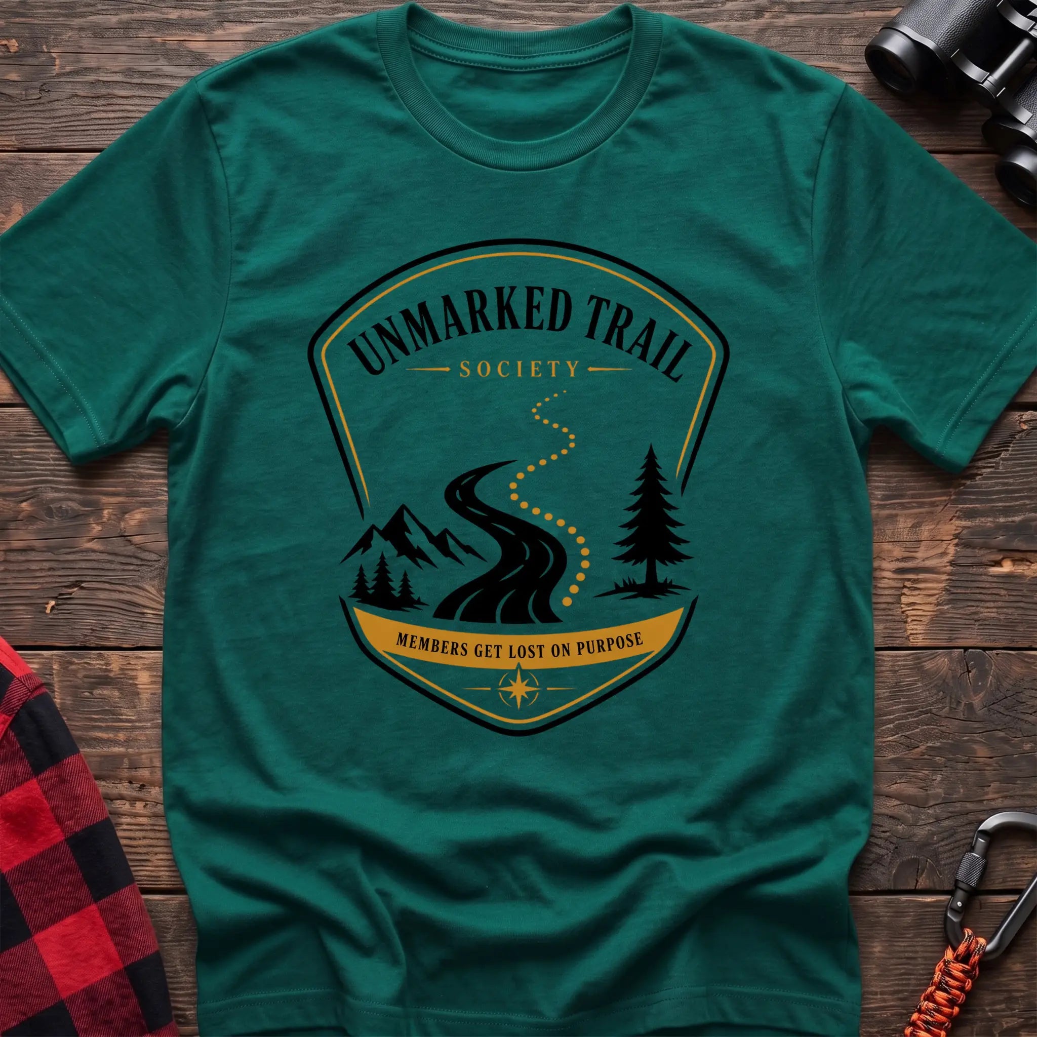Kelly green cotton hiking t-shirt with Unmarked Trail Society badge, winding trail, mountains, pine trees, and "Members Get Lost on Purpose" text
