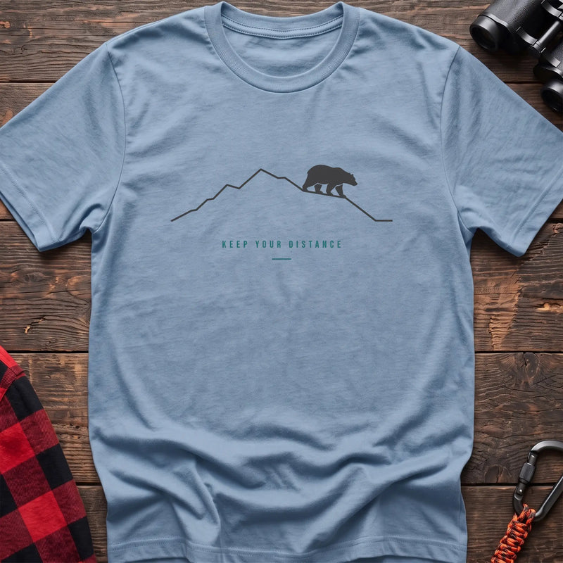 Light blue hiking t-shirt with a line-art mountain, walking bear, and the text “Keep Your Distance”