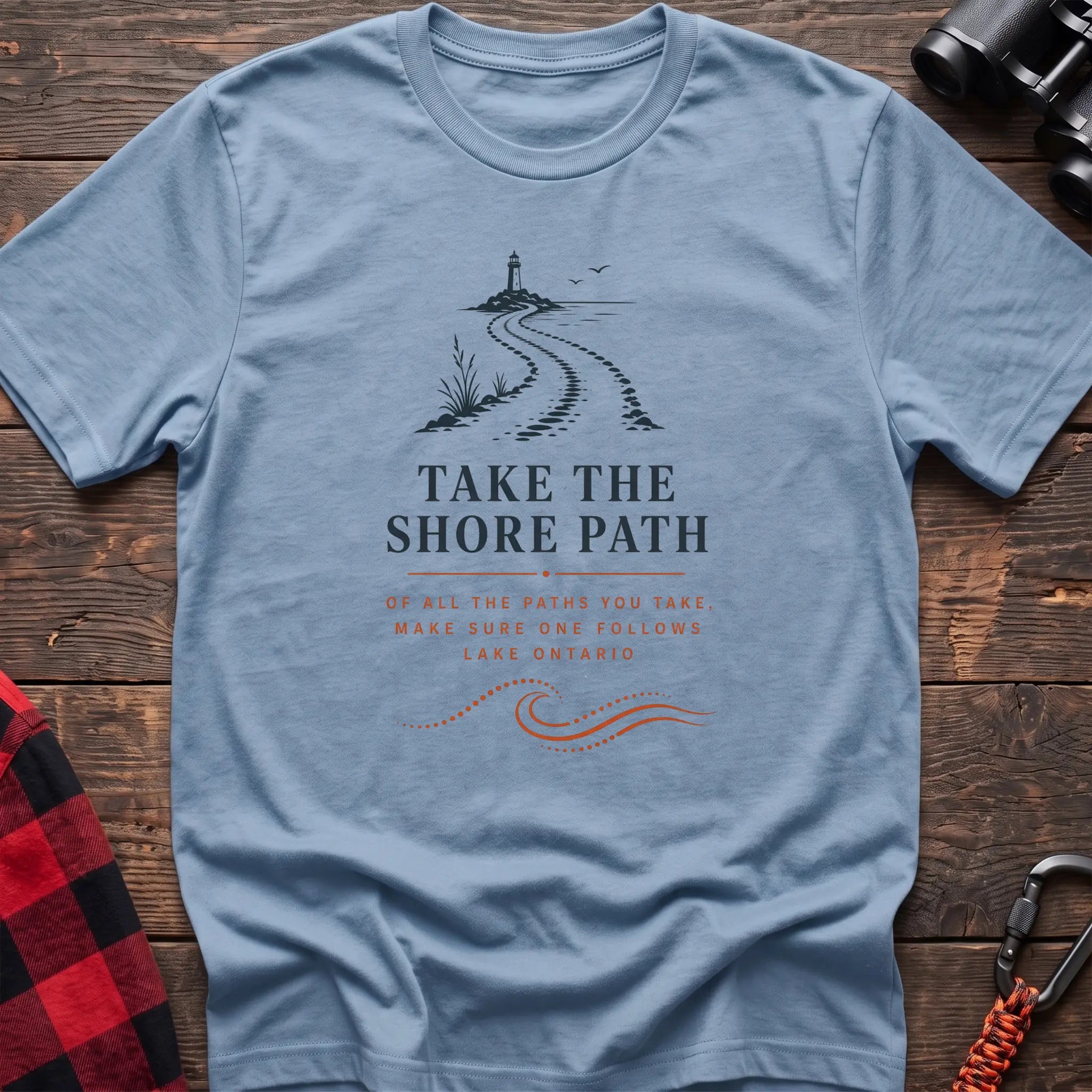 Light blue cotton hiking t-shirt with lighthouse and winding shore path graphic and "Take the Shore Path – make sure one follows Lake Ontario" quote