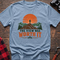 Light blue cotton t-shirt with a hiker on a mountain sunset graphic and The View Was Worth It text on rustic wood