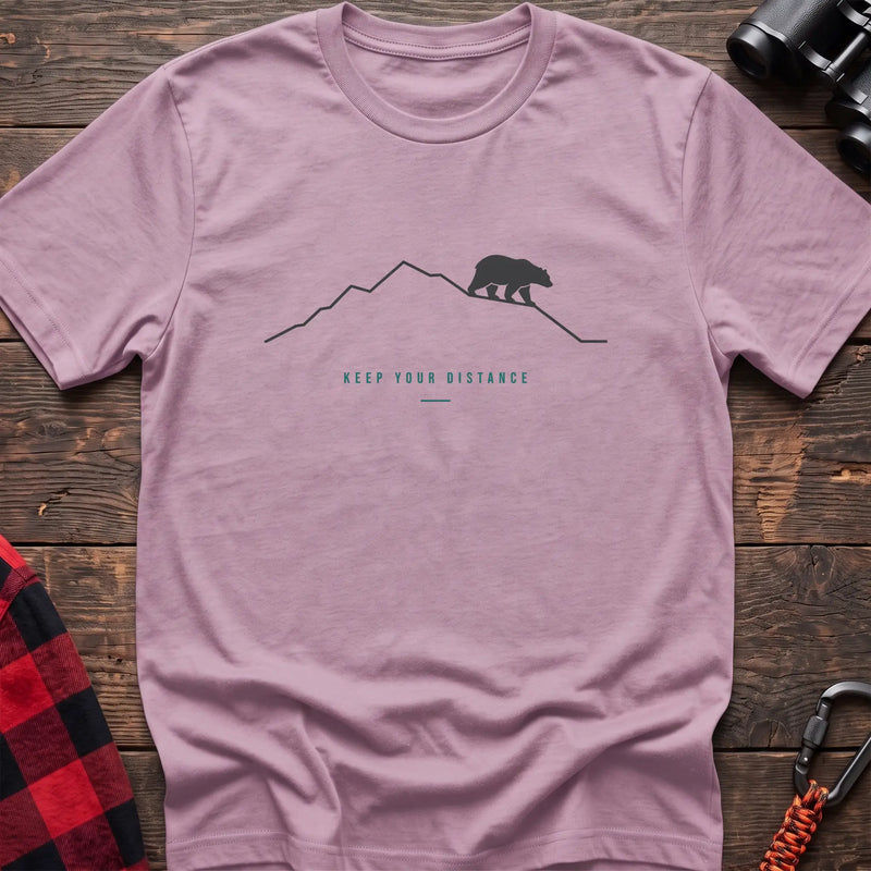 Light pink hiking t-shirt with a line-art mountain, walking bear, and the text “Keep Your Distance”