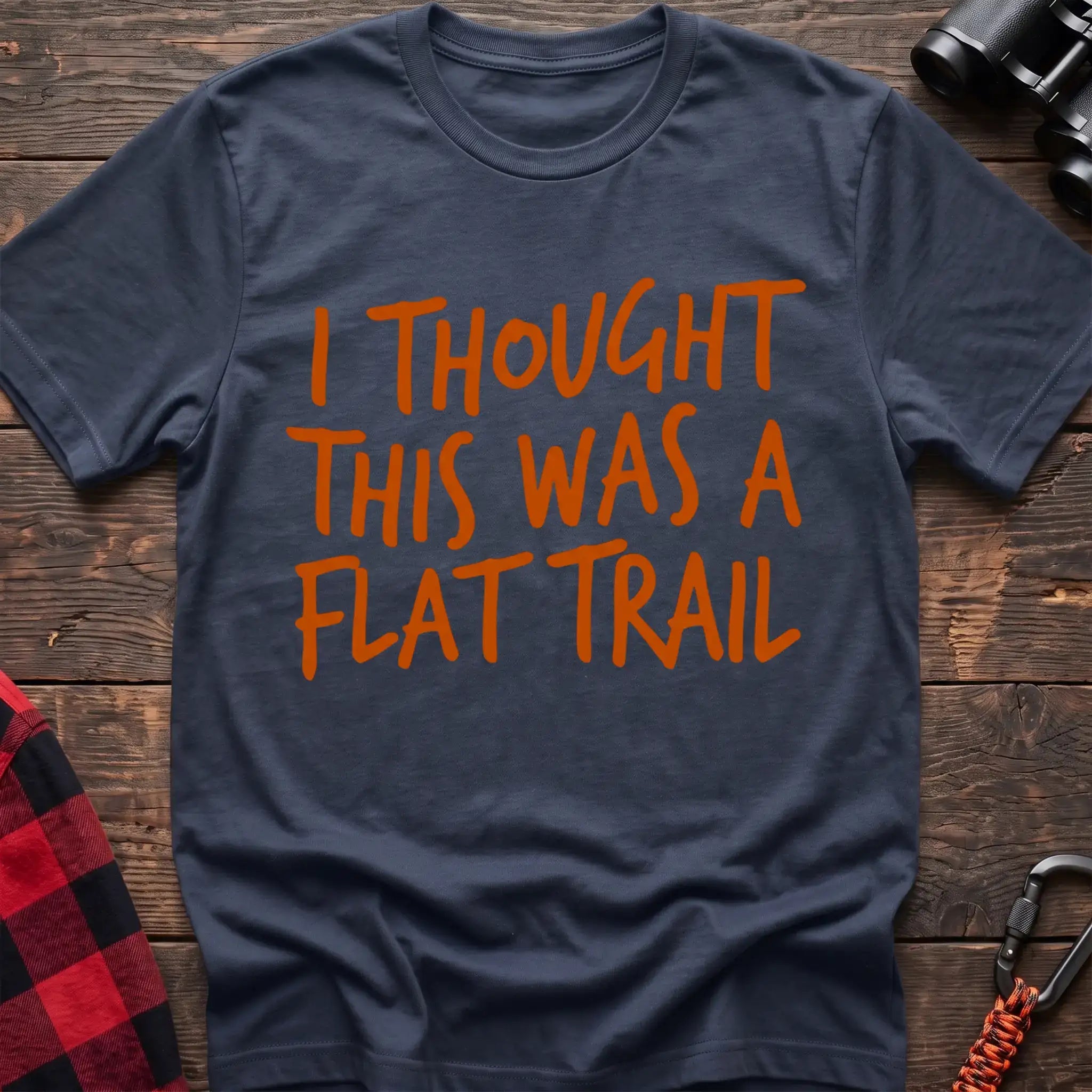 Navy t-shirt with bold orange handwritten-style text reading “I THOUGHT THIS WAS A FLAT TRAIL,” laid flat on a wooden surface.