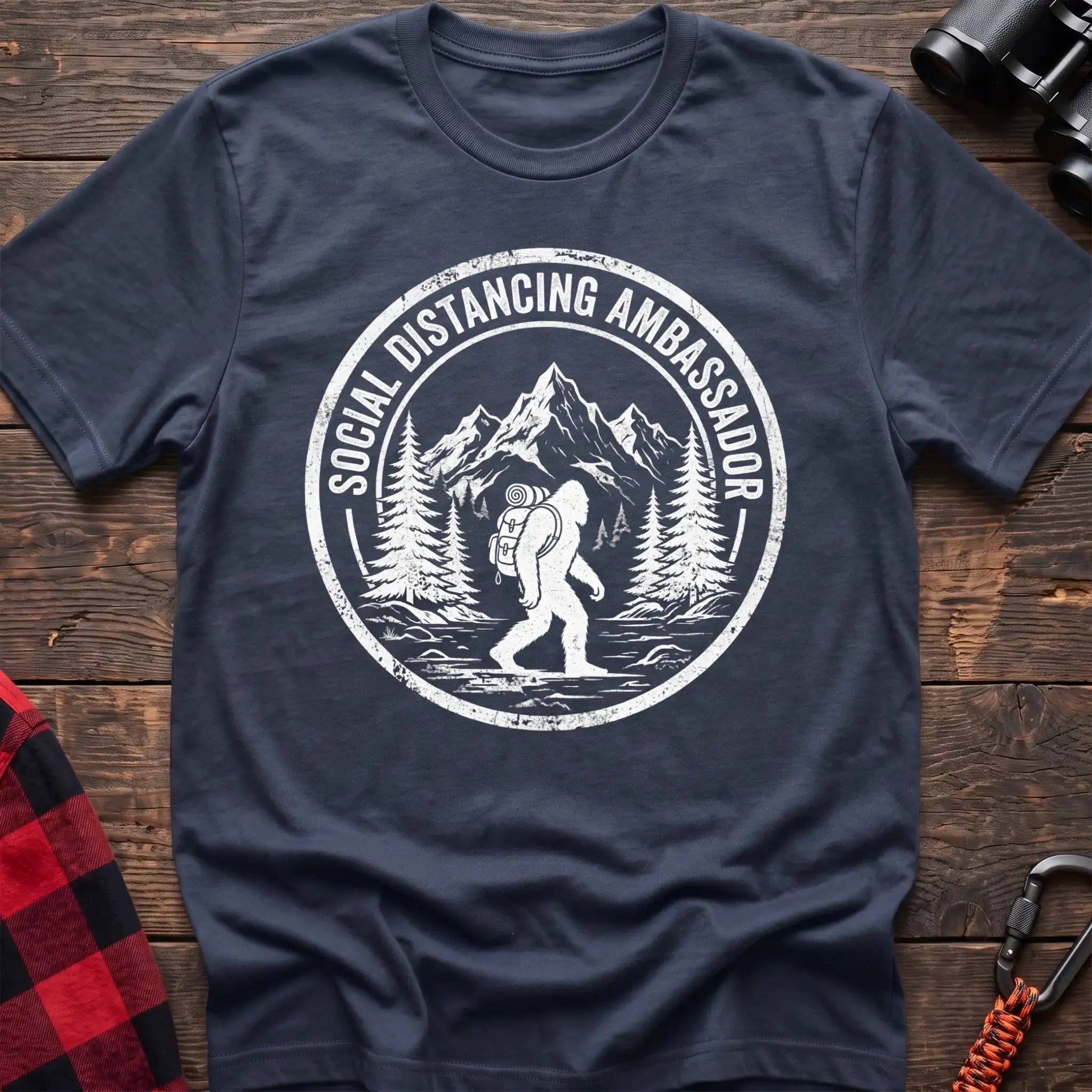 Navy t-shirt with white circular badge graphic of Bigfoot hiking with a backpack through mountains and the text Social Distancing Ambassador