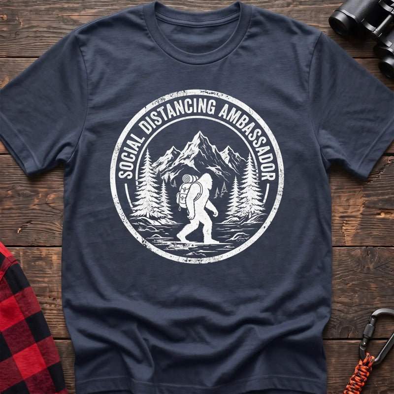 Navy t-shirt with white circular badge graphic of Bigfoot hiking with a backpack through mountains and the text Social Distancing Ambassador