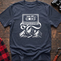 Navy blue t-shirt with white cassette tape graphic labeled Trail Mix Vol. 1, with tape unspooling into a trail through mountains
