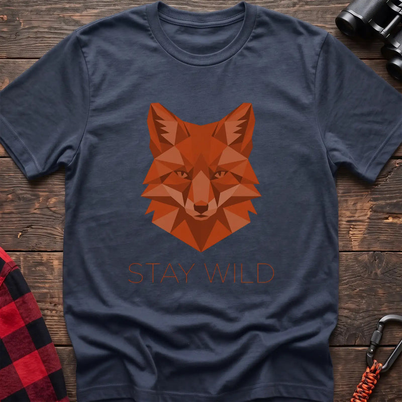 Navy t-shirt with a geometric low-poly orange fox head and the text “STAY WILD” printed below in matching orange, laid flat on a wooden surface.