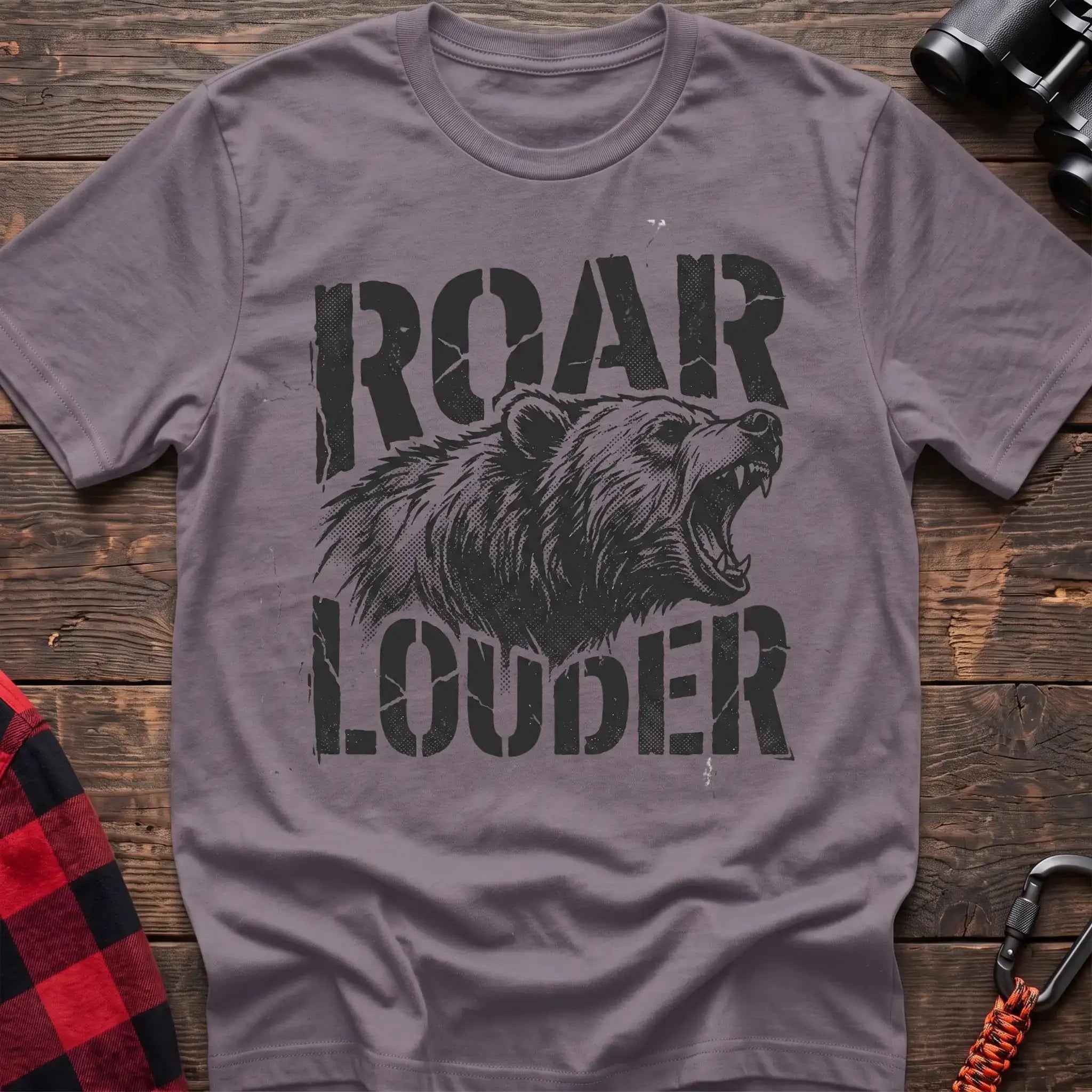 Paragon t-shirt with a distressed black graphic of a roaring bear head between the bold text “ROAR” and “LOUDER,” laid flat on a wooden surface.