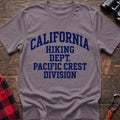 Paragon t-shirt with distressed blue collegiate-style text reading “CALIFORNIA HIKING DEPT. PACIFIC CREST DIVISION,” laid flat on a wooden surface.