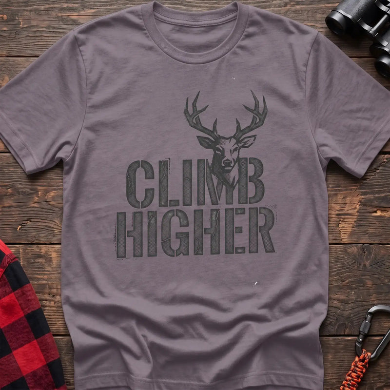 Paragon t-shirt with a distressed dark graphic of a deer’s head and antlers rising from the bold text “CLIMB HIGHER,” laid flat on a wooden surface.