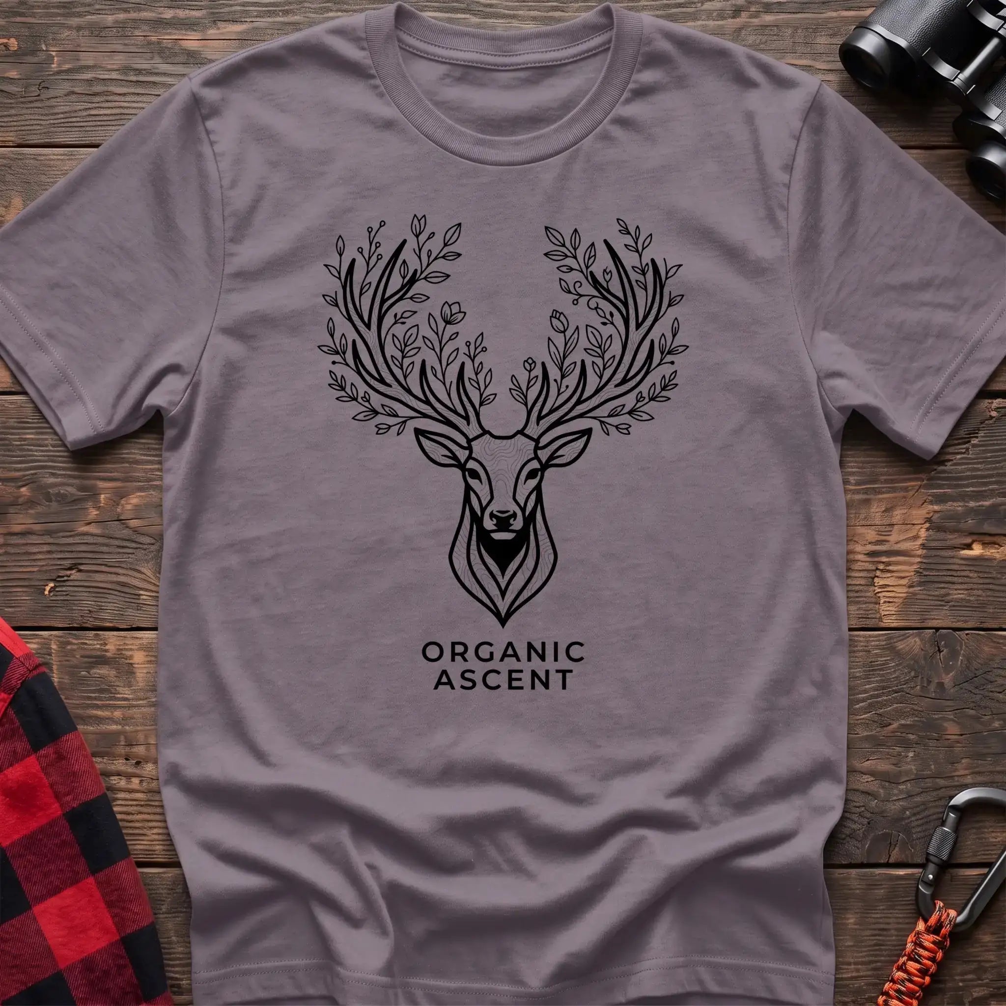 Paragon t-shirt with a black line drawing of a deer’s head whose antlers are formed from leafy branches and flowers, with the text “ORGANIC ASCENT” printed below, laid flat on a wooden surface.