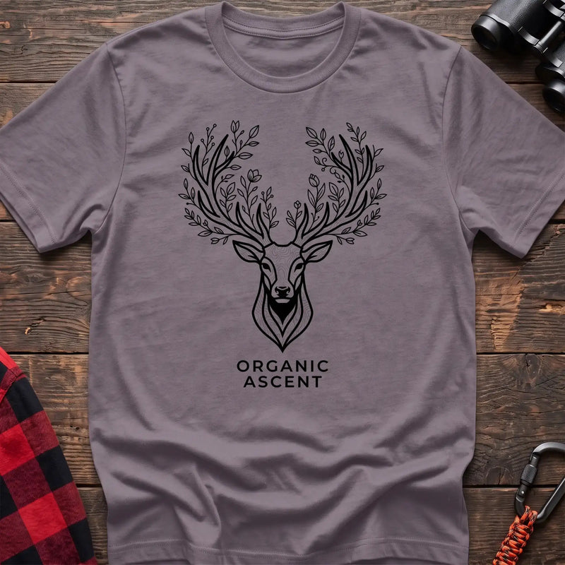 Paragon t-shirt with a black line drawing of a deer’s head whose antlers are formed from leafy branches and flowers, with the text “ORGANIC ASCENT” printed below, laid flat on a wooden surface.