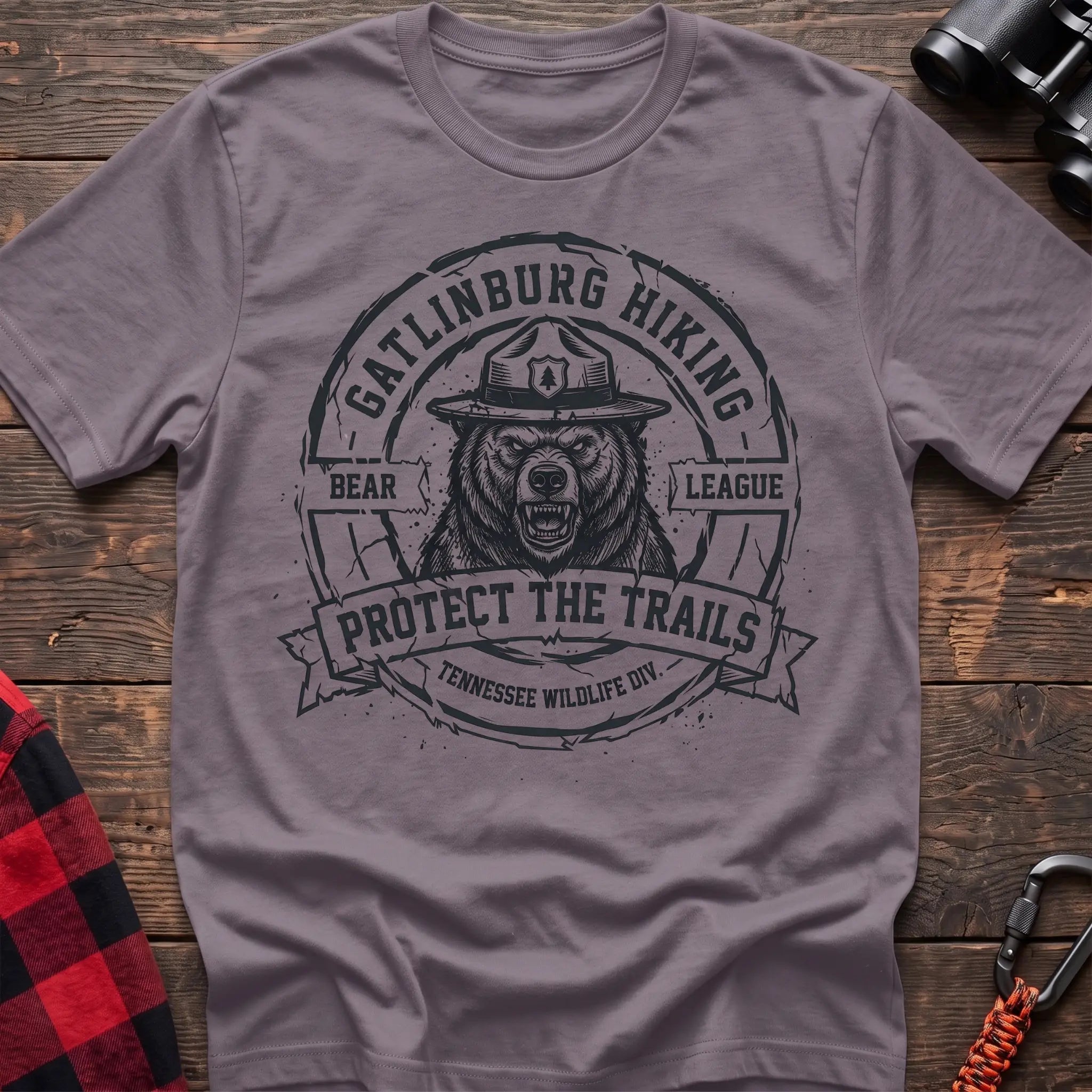 Paragon cotton t-shirt with vintage Gatlinburg Hiking Bear League graphic of a roaring bear in a park ranger hat, Protect the Trails Tennessee Wildlife Division badge, flat lay on rustic wood with hiking gear