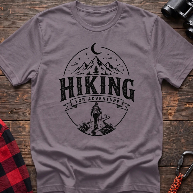 Paragon cotton t-shirt with vintage Hiking for Adventure graphic of mountains under a crescent moon and a hiker on a trail, flat lay on rustic wood with hiking gear